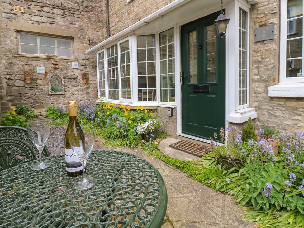 An outdoor area with a table, chairs, a bottle and glasses at Wedgewood Cottage in Middleham
