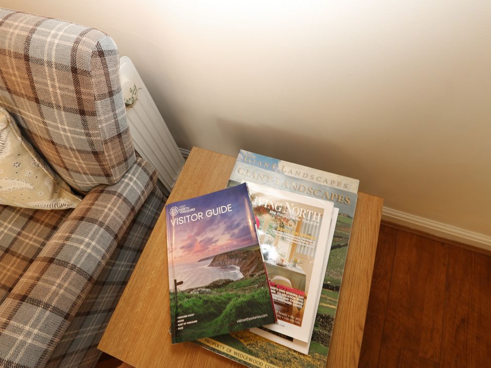 A living room with an armchair and magazines on a side table at Wedgewood Cottage in Middleham
