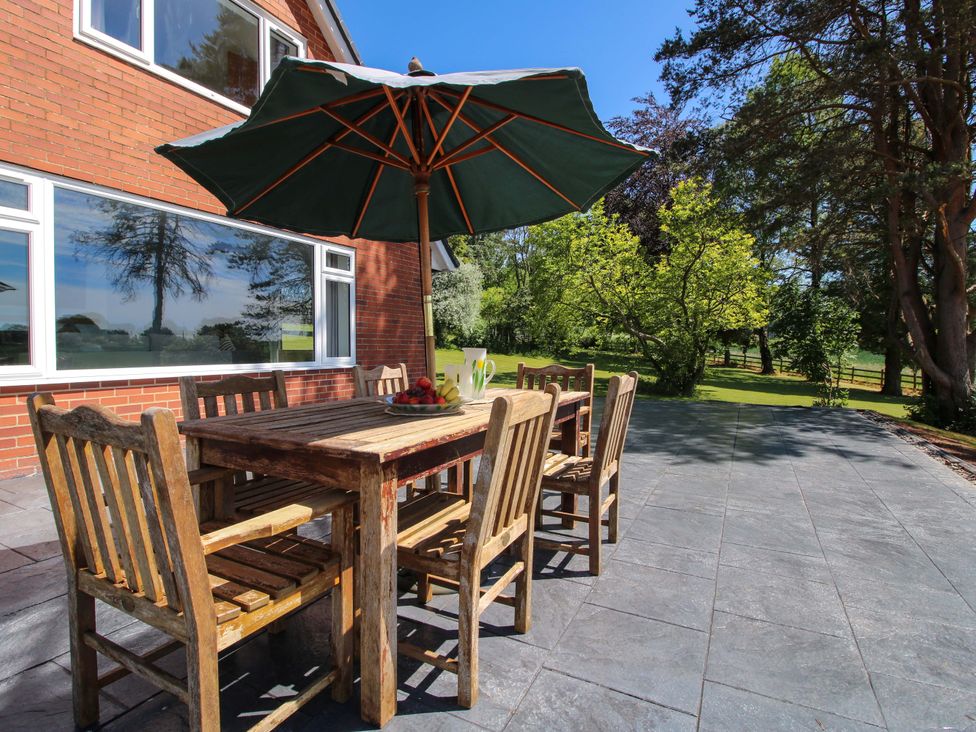 A patio with a wooden table and chairs under an umbrella at Westington Hall in Hatfield near Bromyard
