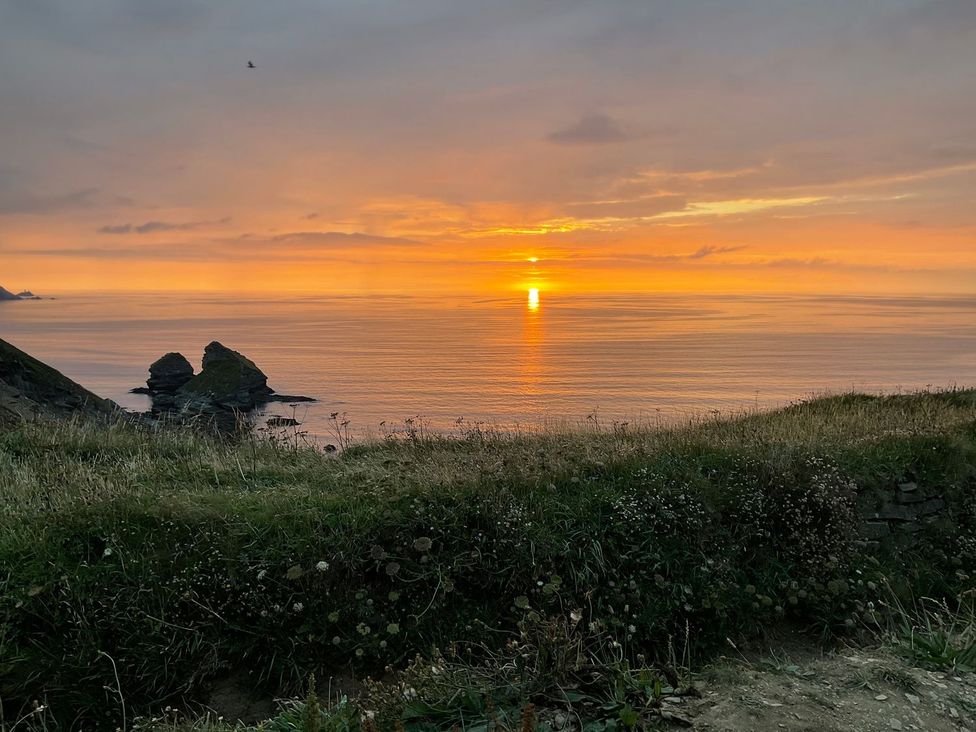 A sunset over the ocean with rocks in the foreground at Warleggan in Portreath