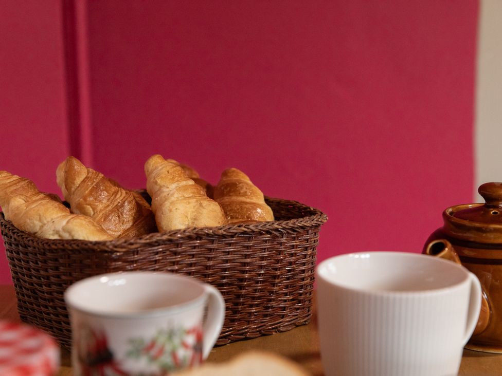 A basket of croissants with cups and a teapot at Bishop Lightfoot Cottage in Bishop Auckland