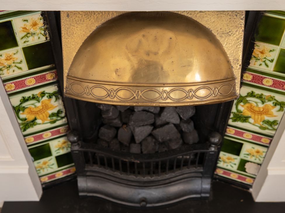 A fireplace with a brass cover and decorative tiles at Bishop Lightfoot Cottage in Bishop Auckland