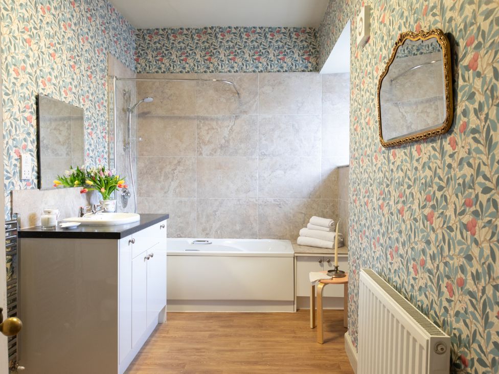 A bathroom with a bath tub, shower, sink, and mirror at Bishop Lightfoot Cottage in Bishop Auckland