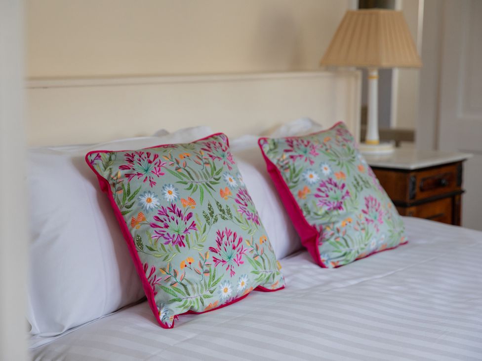 A bed with floral pillows and a bedside lamp at Bishop Lightfoot Cottage in Bishop Auckland
