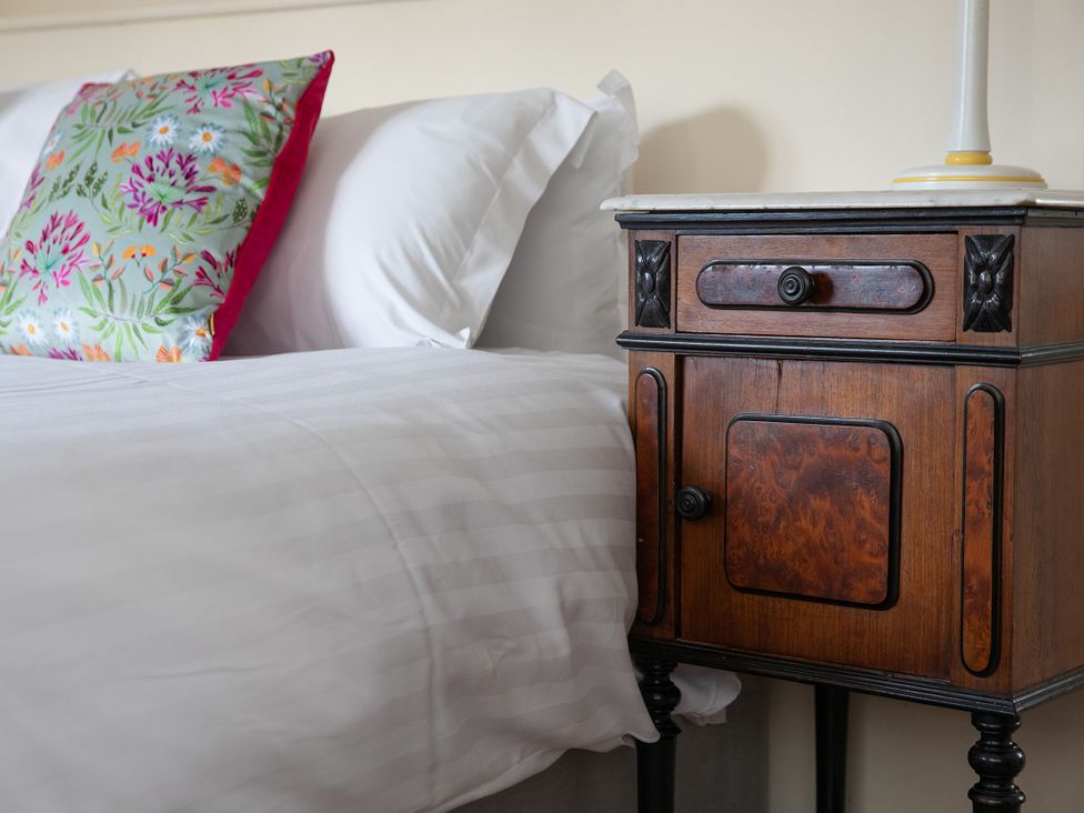 A bed with a floral pillow and a wooden nightstand with a lamp at Bishop Lightfoot Cottage in Bishop Auckland