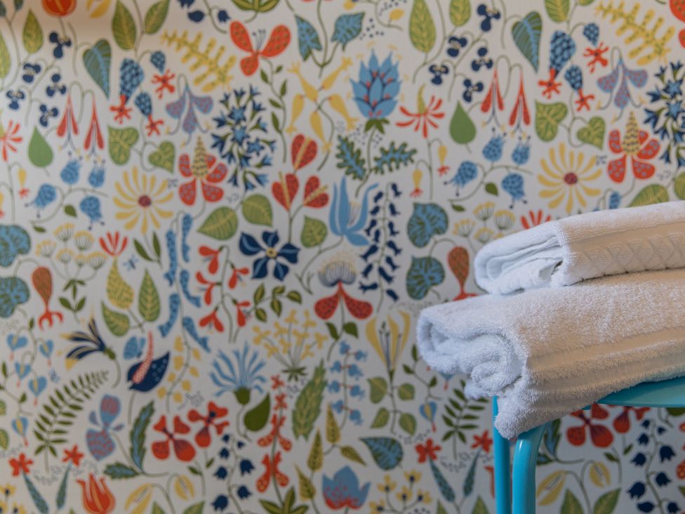 A stack of towels on a blue stool with floral patterned wallpaper at Sheriff's Tower Cottage - East Bishop Auckland