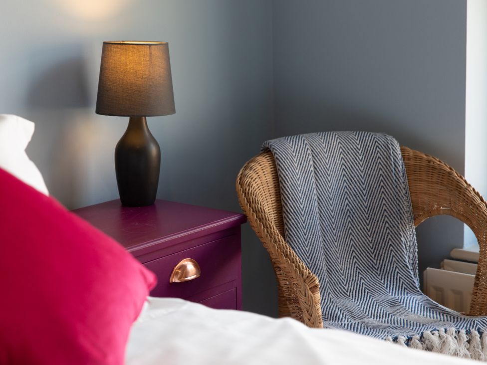 A bedroom with a lamp and wicker chair at Sheriff's Tower Cottage - West in Bishop Auckland