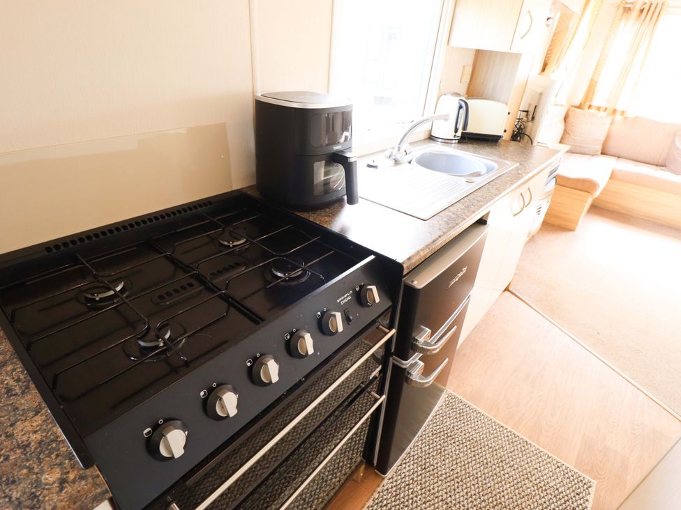 A kitchen with a gas stove, sink, kettle, and fridge at The Seafront Cosy Caravan in Ingoldmells