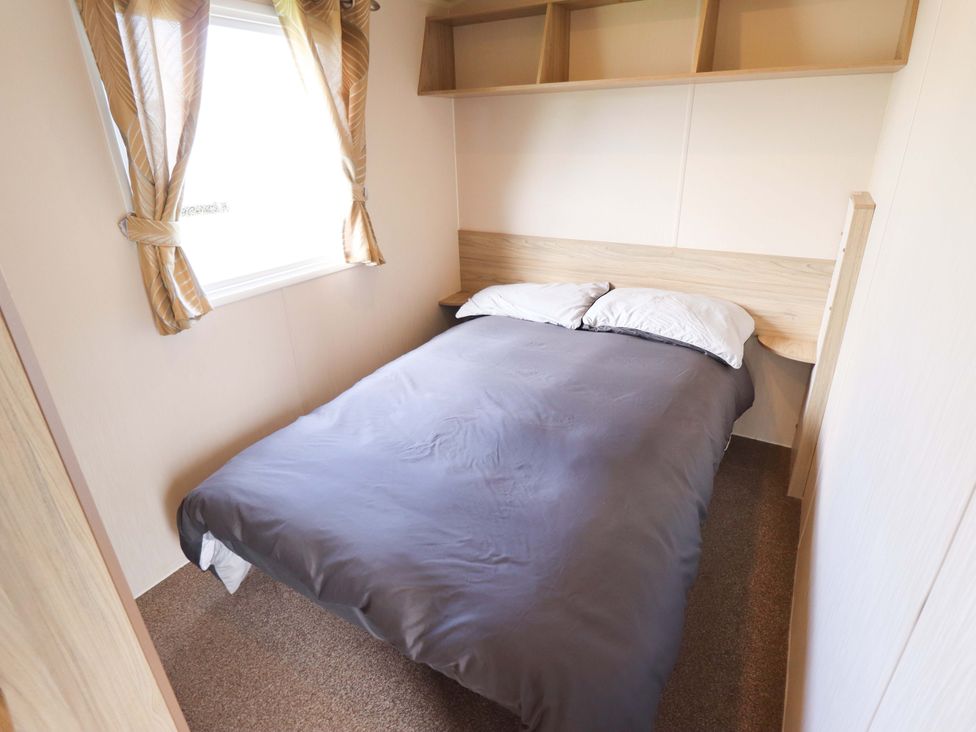 A bedroom with a bed and shelves at The Seafront Cosy Caravan Ingoldmells