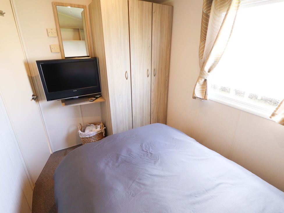 A bedroom with a bed, television, wardrobe, and mirror at The Seafront Cosy Caravan in Ingoldmells