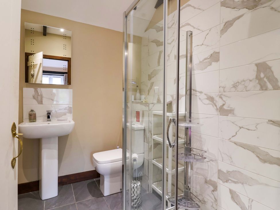 A bathroom with a shower, sink, toilet, and mirror at Cider Press Cottage in Torpoint