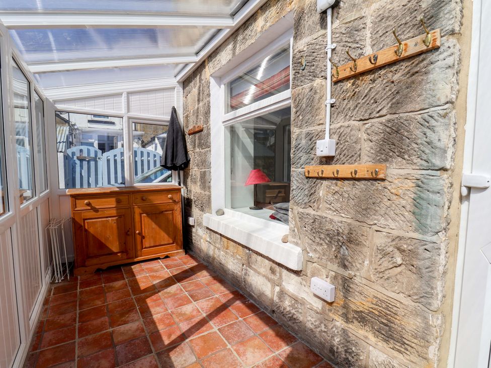 A conservatory with a wooden cabinet and coat hooks at Cozy Cottage
