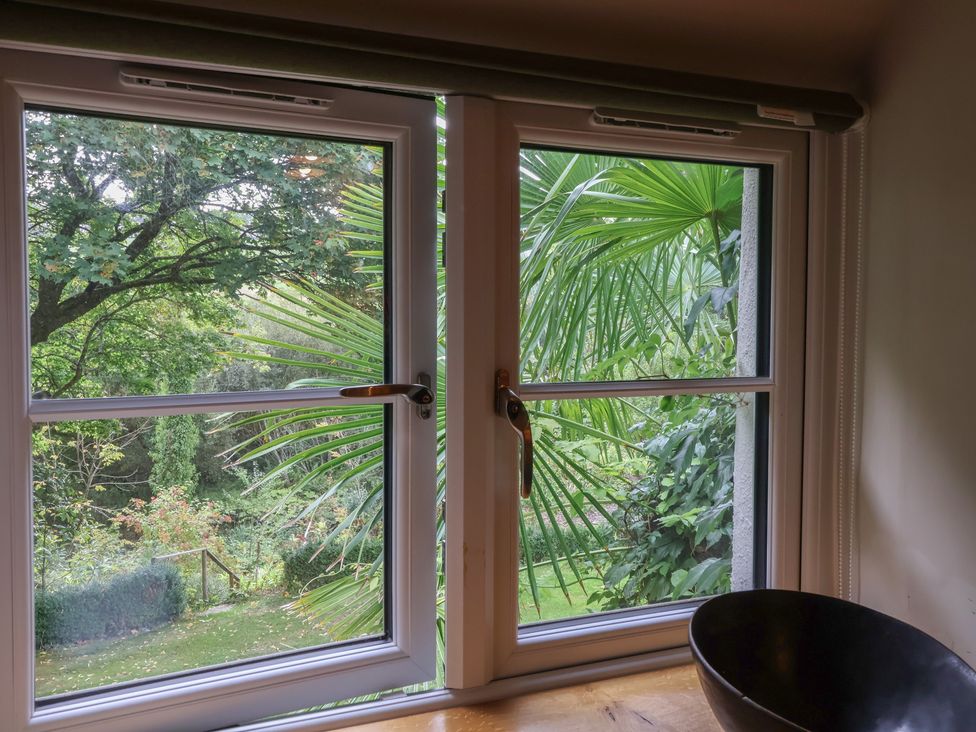 A window overlooking a garden with trees and plants at The Bothy at Lewis Cottage Spreyton