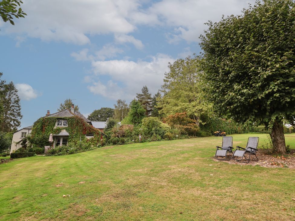 An outdoor photo of a house and lawn with chairs at The Bothy at Lewis Cottage Spreyton