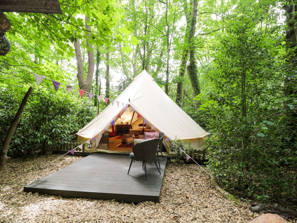 A glamping tent with wooden platform and outdoor seating at Bedouin Bell Tent in Woolton Hill