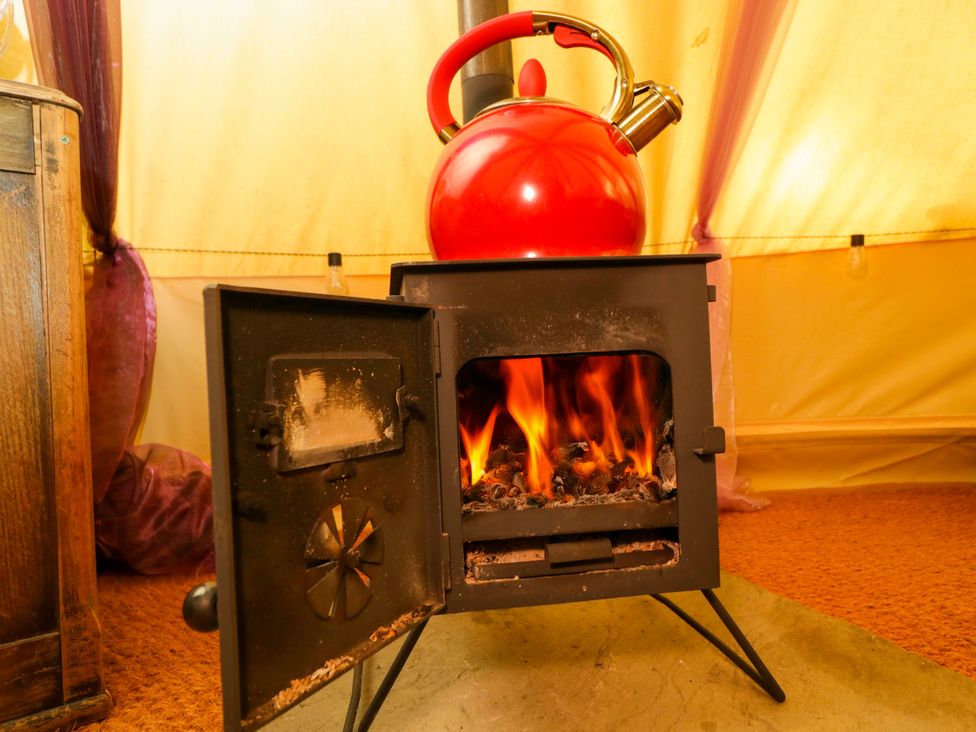 A wood stove with flames and a kettle on top at Bedouin Bell Tent in Woolton Hill