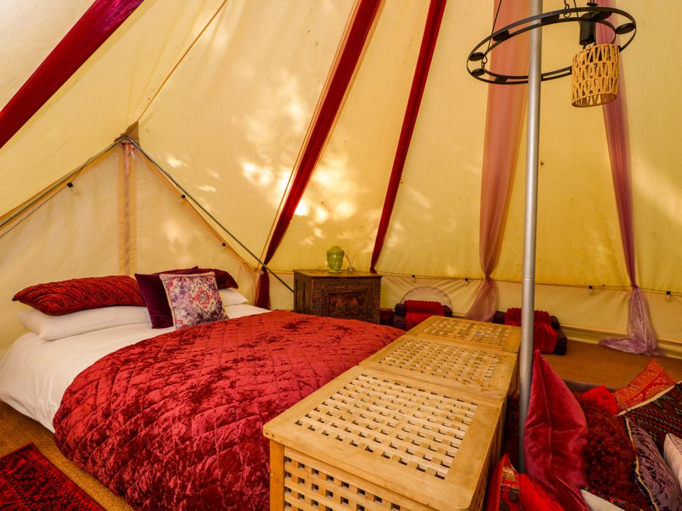 A bedroom with a bed, side table, and decorative items at Bedouin Bell Tent in Woolton Hill