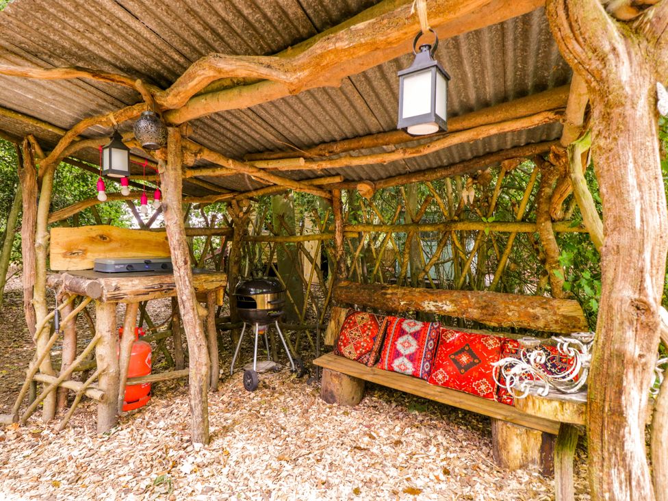 An outdoor cooking area with a grill and wooden table at Bedouin Bell Tent in Woolton Hill