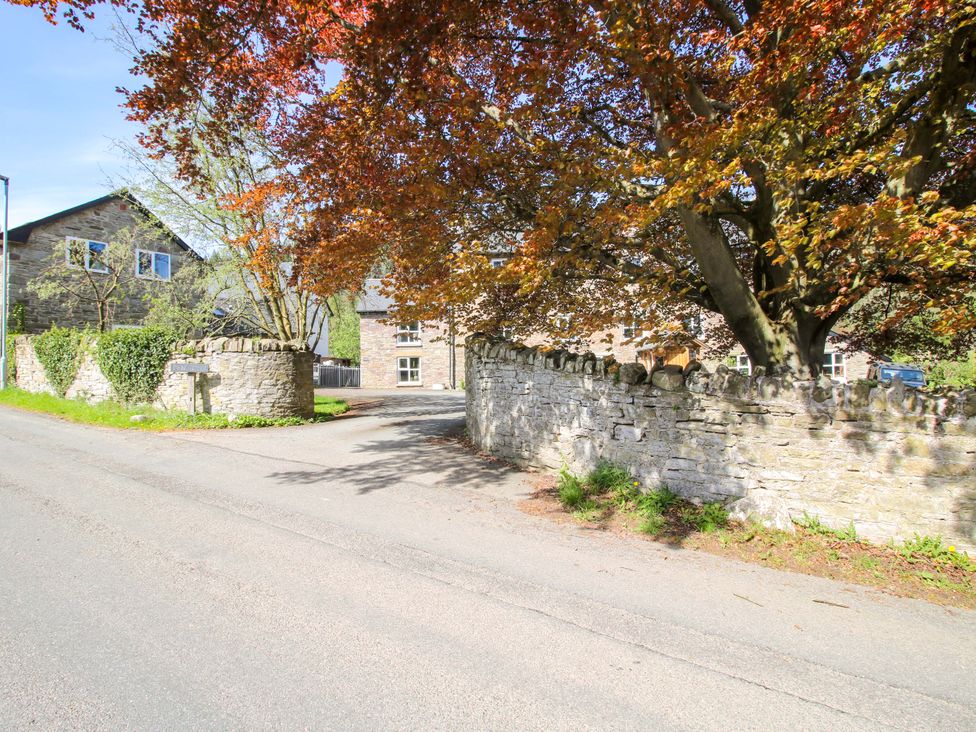 A view of a road with a stone wall and trees at Little Pentwyn in Clyro
