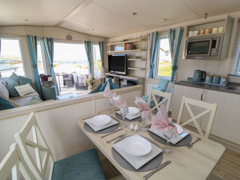 A living room with a dining area and kitchen appliances at Swanny View in Swanage