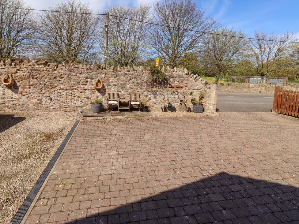 An outdoor area with stone wall and wooden chairs at Willow cottage in Seahouses
