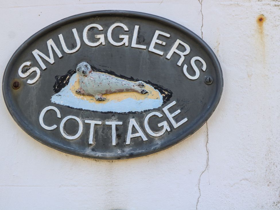 A sign displaying the name Smugglers Cottage with a seal drawing