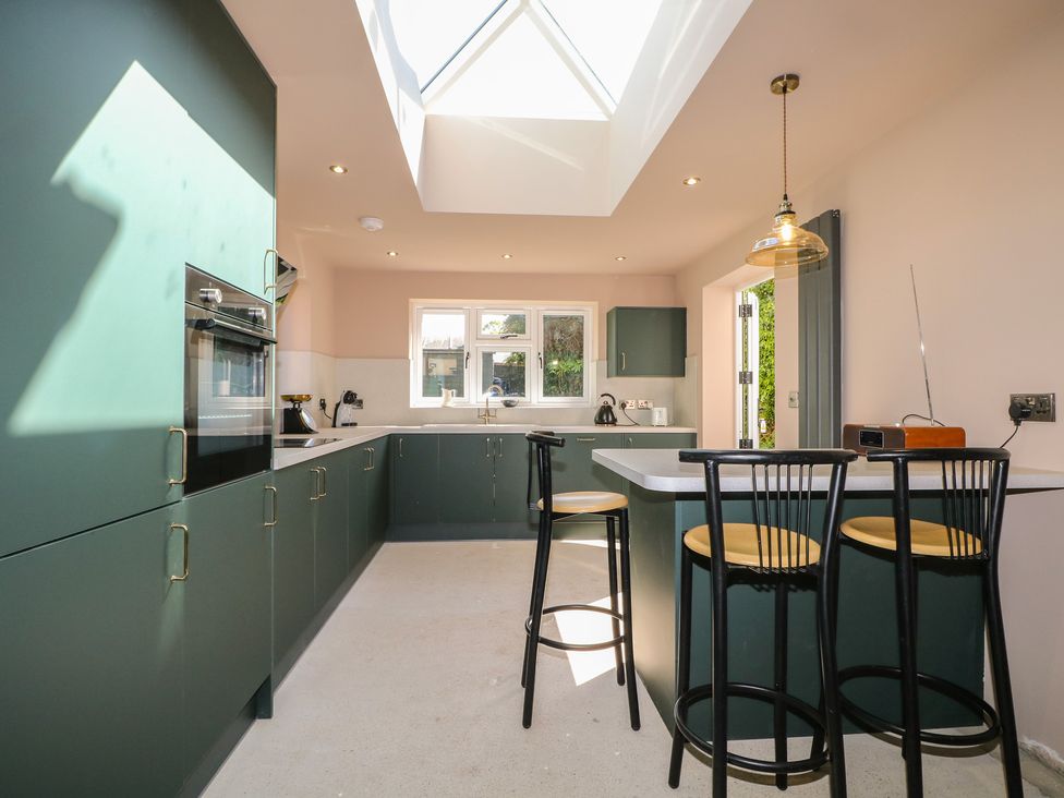 A kitchen with cabinetry and bar stools at Smugglers Cottage in Selsey
