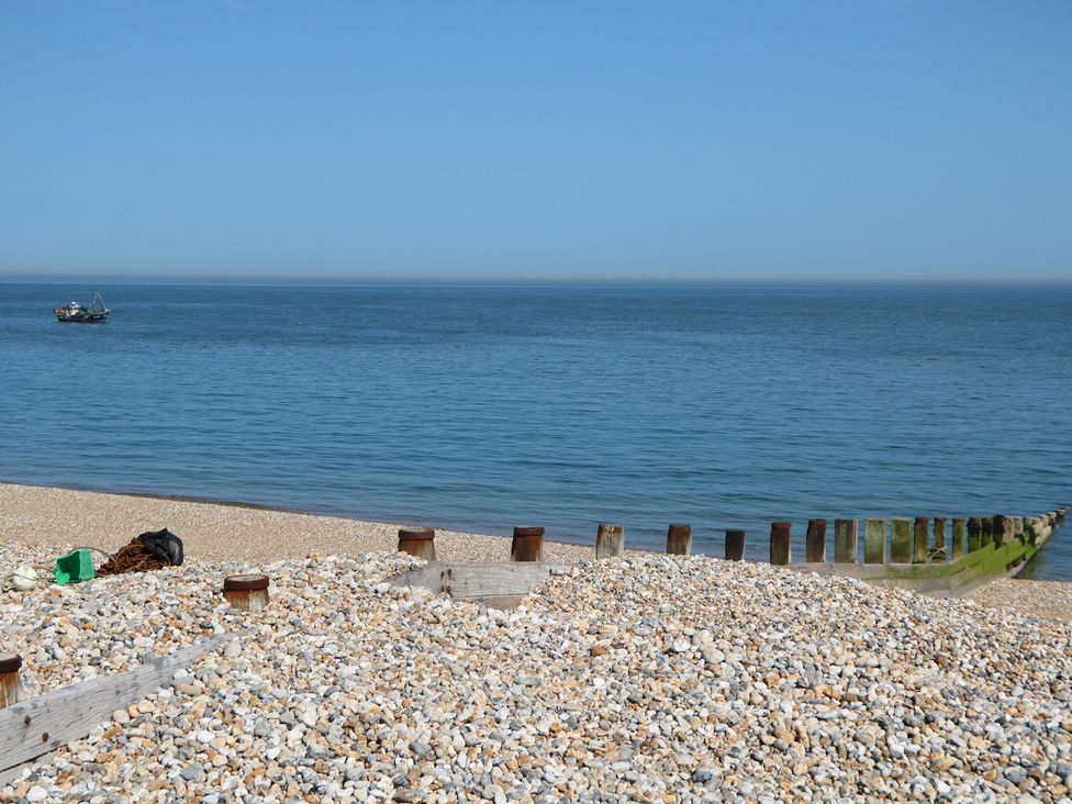 A beach with pebbles and a boat on the water at Smugglers Cottage Selsey