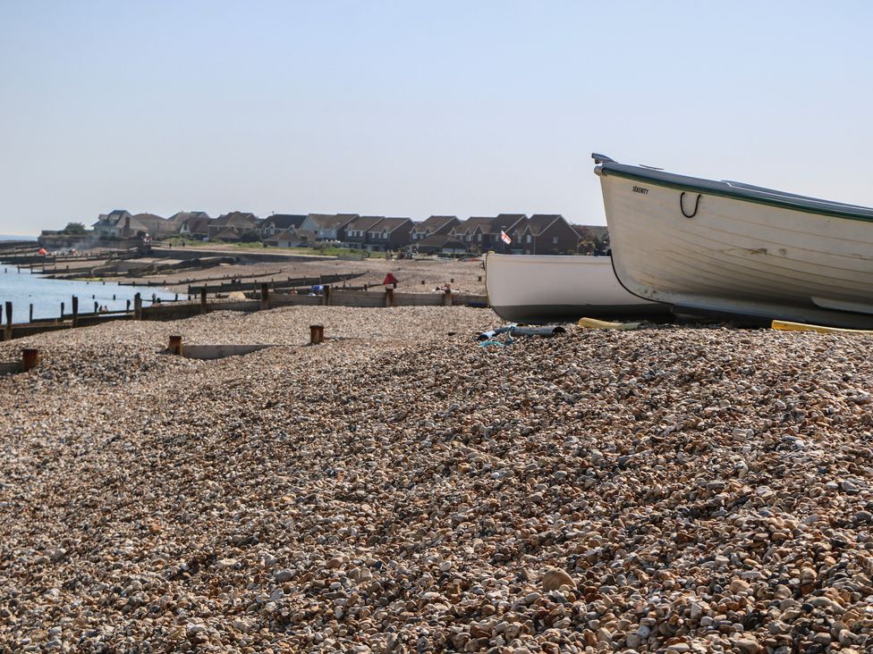 A beach with boats on pebbles and houses in the background at Smugglers Cottage in Selsey