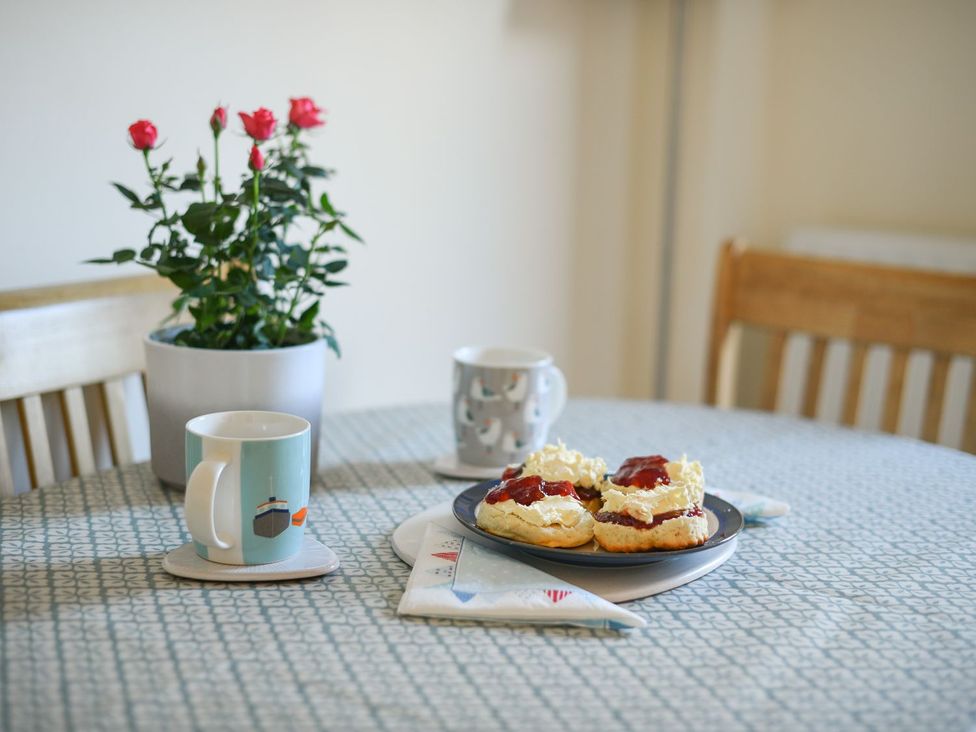 A kitchen table with scones, mugs, and a flower pot at Mead Cottage in Bridport