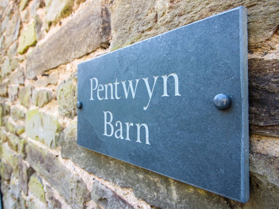A sign displaying Pentwyn Barn attached to a stone wall in Clyro