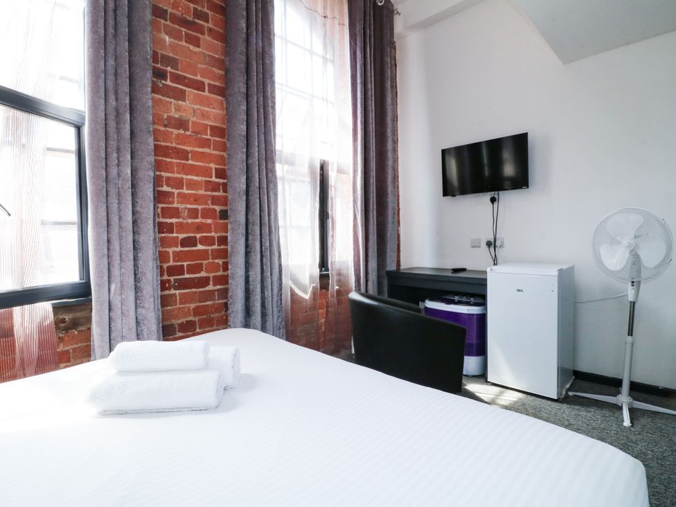 A bedroom with a bed, towels, desk, television, and mini fridge at Apartment 304 Nottingham