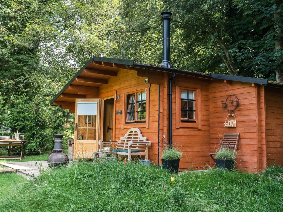 A cabin with a wooden porch and outdoor furniture at Cabin for 2 - Wood Burning Hot Tub & Fire in Larkhall