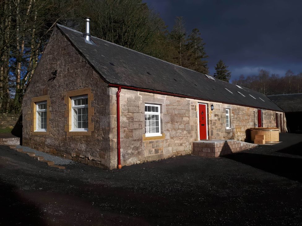 An outdoor view of a stone building with red doors at 2-Bed Barn, Hot Tub & Pet Friendly near Muirkirk