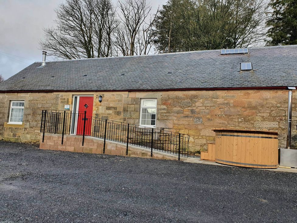 An outdoor view of a house with a red door and a hot tub at 2-Bed Barn, Hot Tub & Pet Friendly near Muirkirk