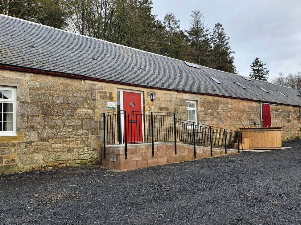 An outdoor view of a building with a red door and a hot tub at 2-Bed Barn, Hot Tub & Pet Friendly near Muirkirk