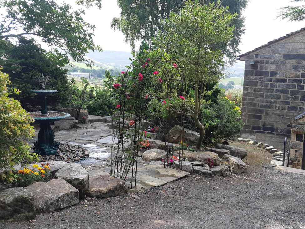 A garden with a fountain, flower beds, and stone pathway at 3 bedroom- Sleeps 6-Greave Farm Todmorden Cottage in Todmorden