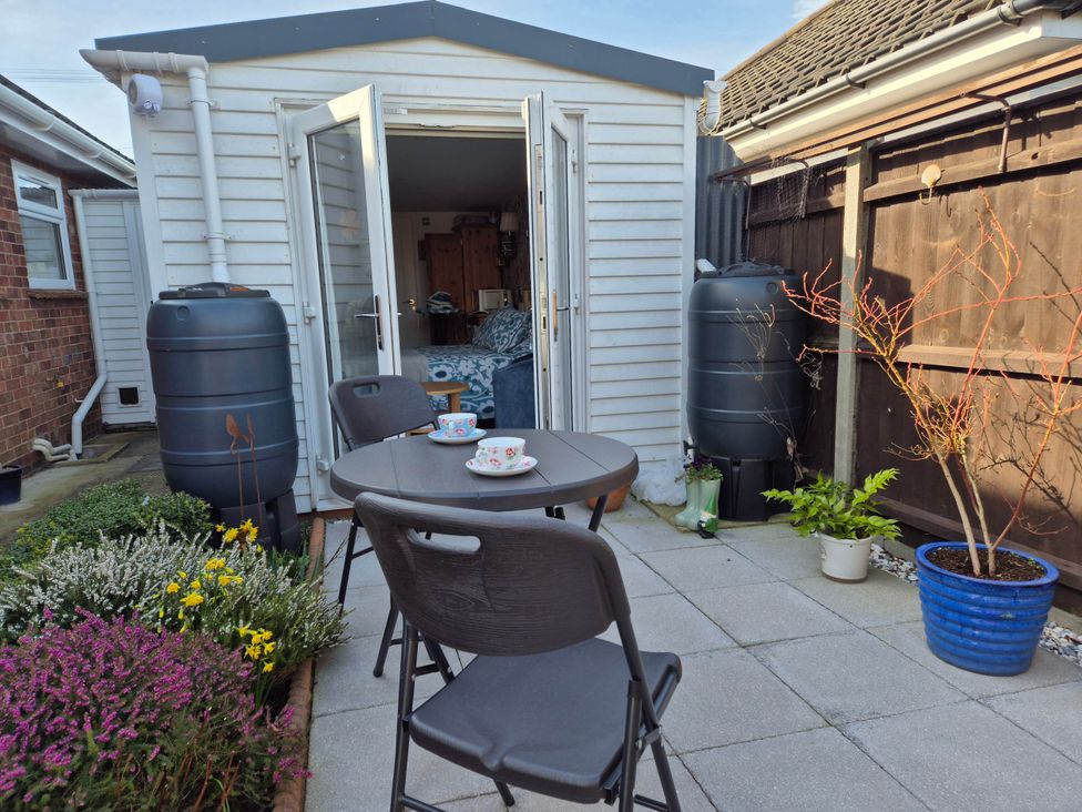 A garden with a table and chairs near a shed and plants at Flower Garden Studio in Sheringham