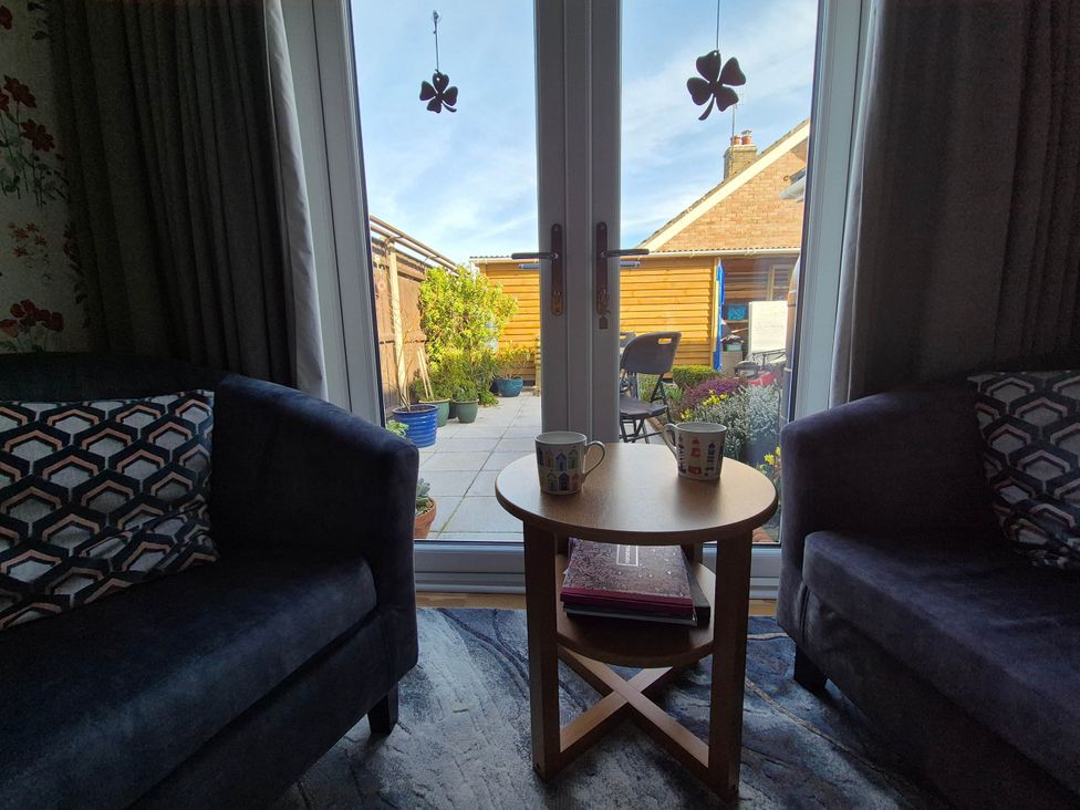 A living room with sofas and a view of a patio at Flower Garden Studio in Sheringham