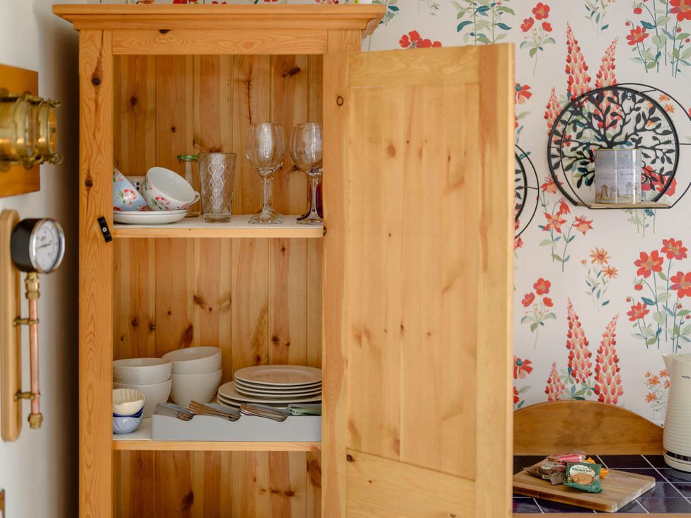 A cupboard with dishes and glasses at Flower Garden Studio in Sheringham