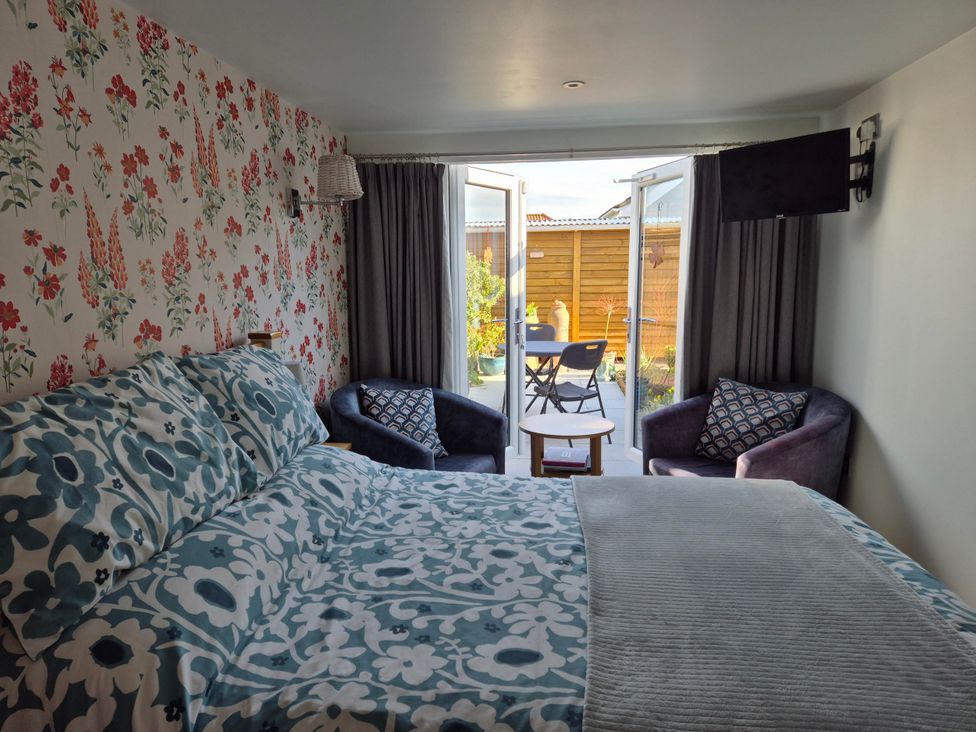 A bedroom featuring a bed, two chairs, and a television at Flower Garden Studio in Sheringham