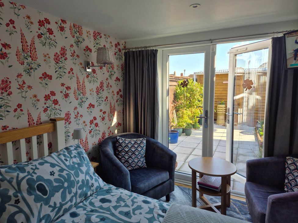 A bedroom with a bed and chairs leading to a garden at Flower Garden Studio in Sheringham