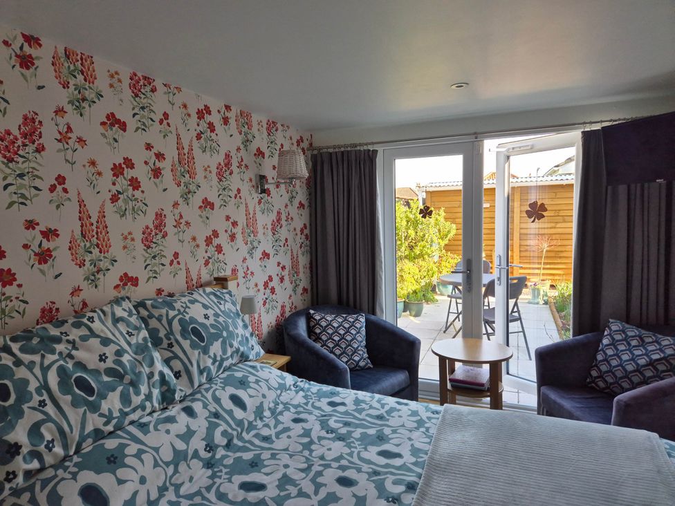 A bedroom with a bed and chairs at Flower Garden Studio in Sheringham