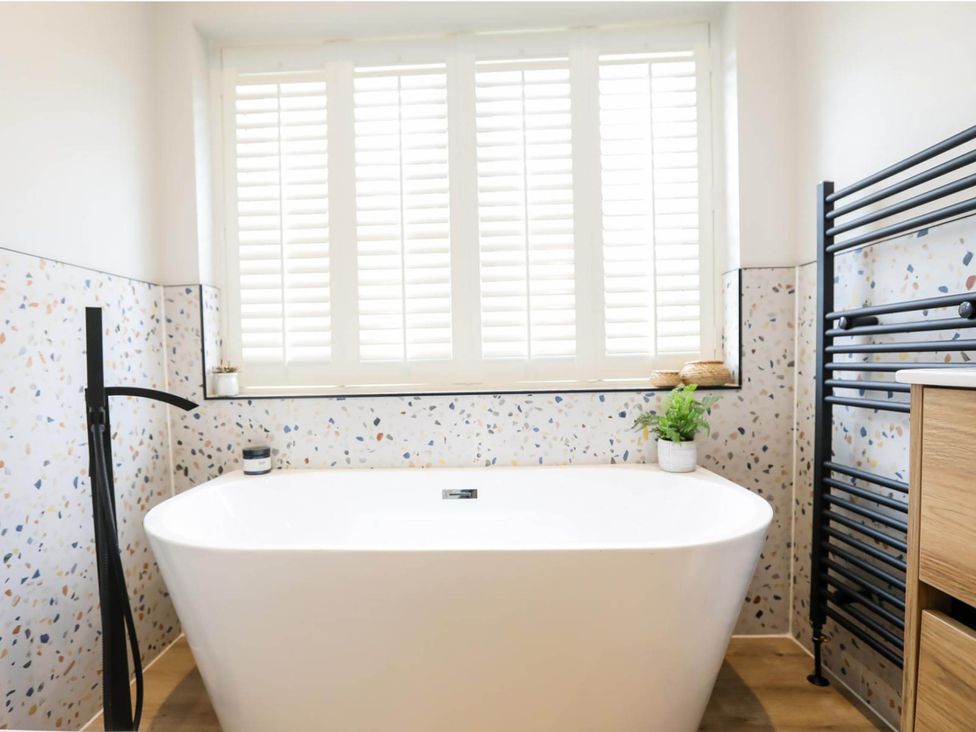 A bathroom with a bathtub, window, and radiator at Luxury 2 Bed Home w/ Spa-like Ensuites & Patio in Hereford