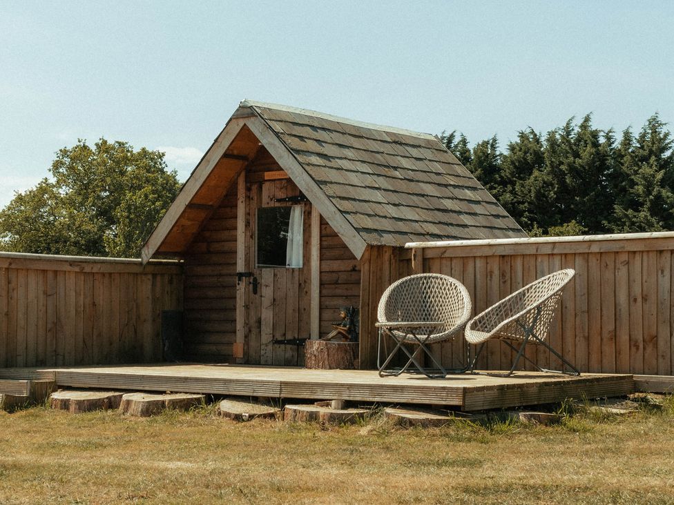 A wooden cabin with a deck and chairs at Glamping at the Retreat Wiltshire in Christian Malford