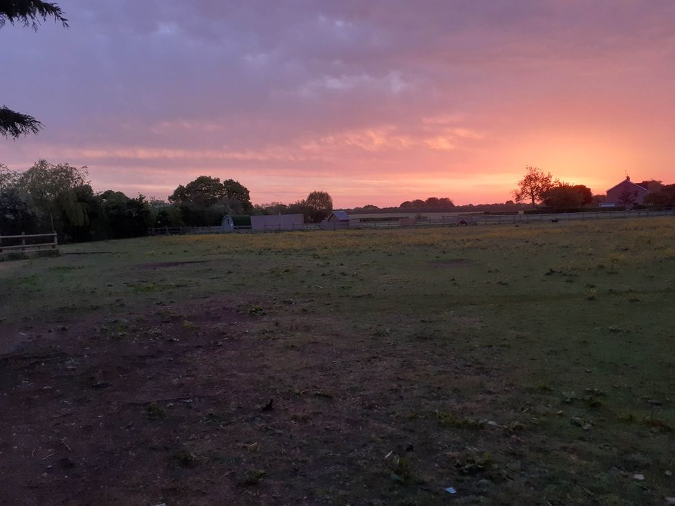 An outdoor view of a field with a sunset at Glamping at the Retreat Wiltshire Christian Malford