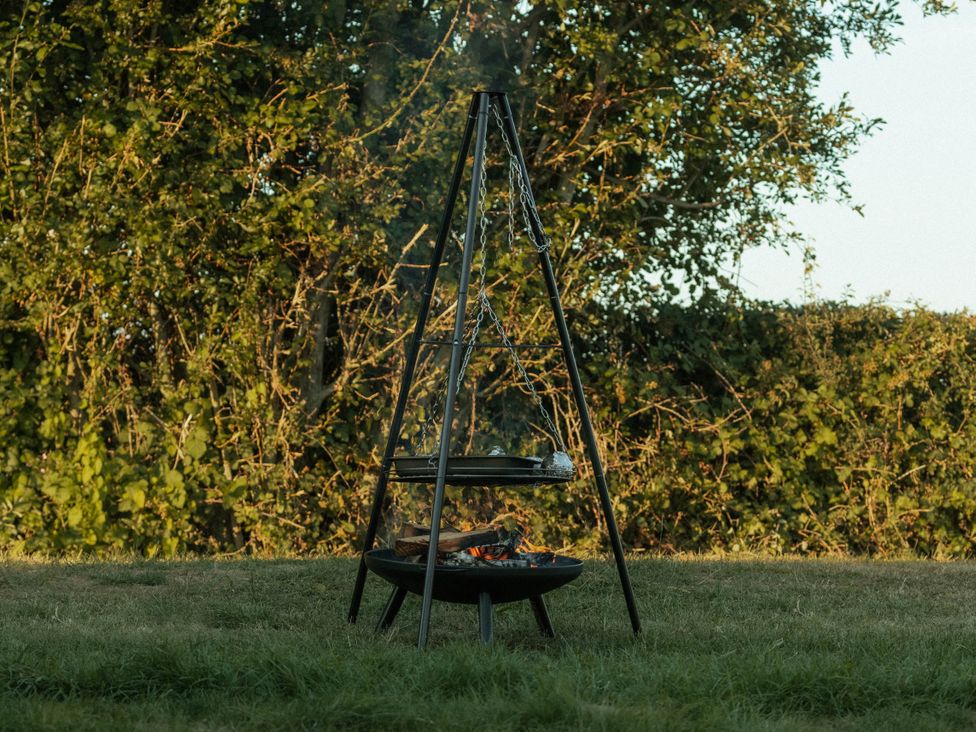 A fire pit with a grill on chains and wood at Glamping at the Retreat Wiltshire in Christian Malford