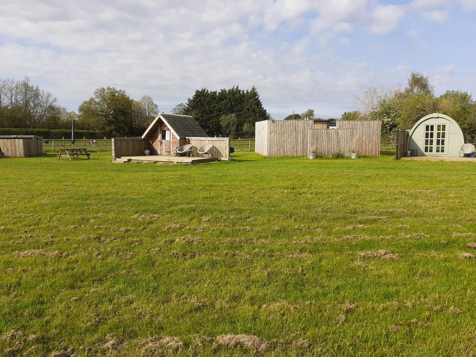An outdoor area with a grassy field and a wooden cabin at Glamping at the Retreat Wiltshire in Christian Malford