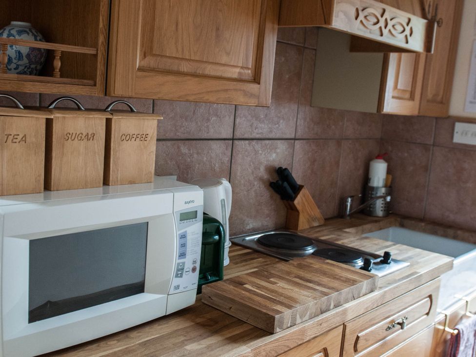 A kitchen with wooden cabinets and a microwave at Beautiful 1-Bed Cottage in Trellech