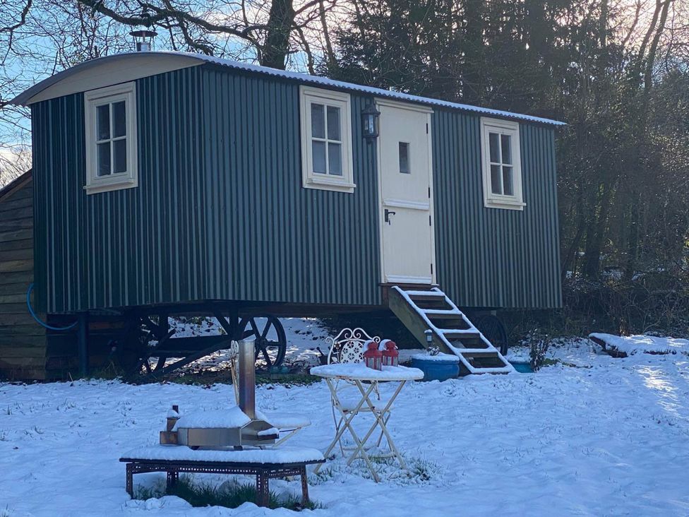 A cabin with wooden steps and a table with chairs in an outdoor area at Cozy Cabin Retreat near Chepstow